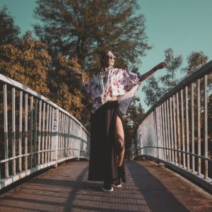 GOLOKA lifestyle photograph of a model in a floral kimono top and sheer black skirt posing on a pedestrian bridge