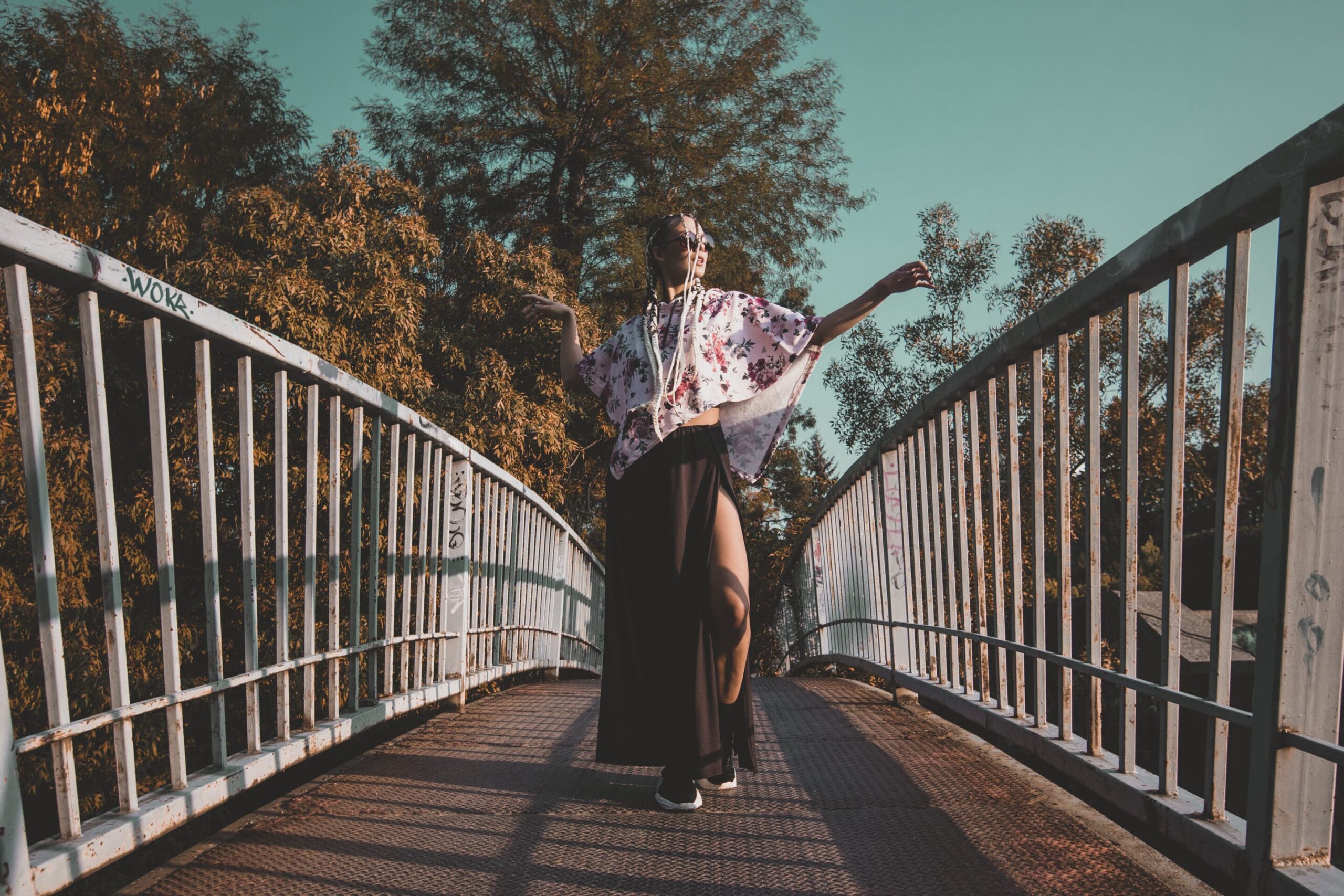 GOLOKA lifestyle photograph of a model in a floral kimono top and sheer black skirt posing on a pedestrian bridge
