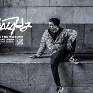GOLOKA homepage hero photograph of a model in a bandana and printed jacket seated on stone steps, black and white urban style