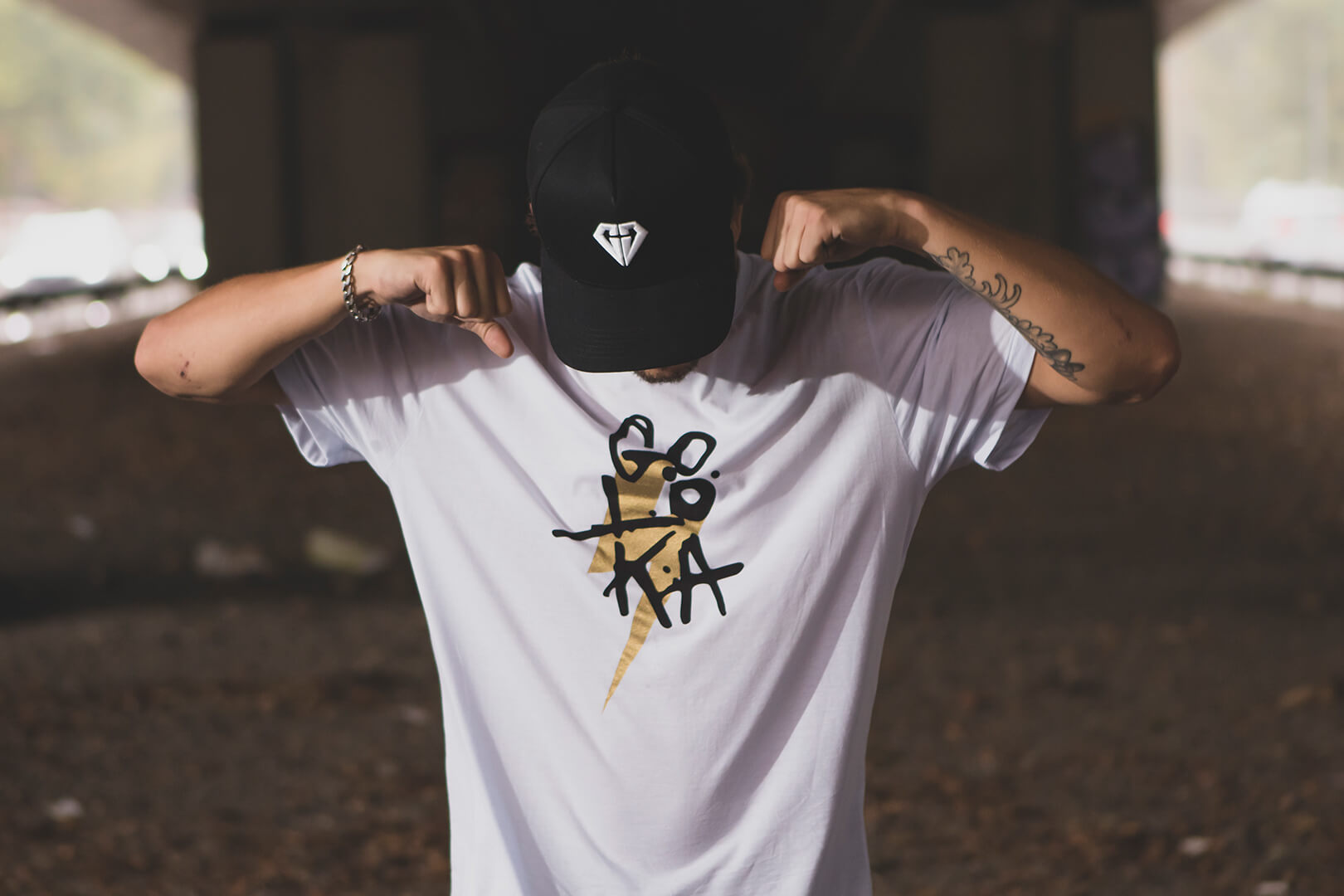 GOLOKA Accessories category: model wearing a black diamond-logo cap and white graphic t-shirt under a bridge