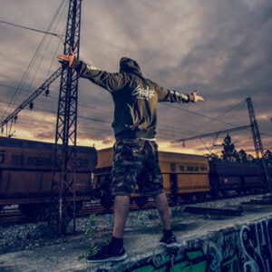 GOLOKA High Voltage collection lookbook cover: model in an olive hoodie and camo shorts standing on train tracks at sunset