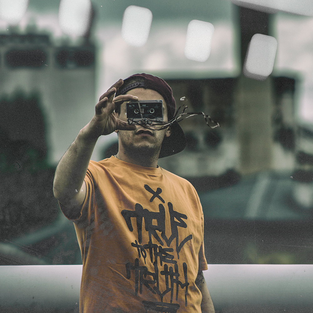 GOLOKA True to the Truth lookbook cover: model in a mustard graphic t-shirt holding a vintage camera